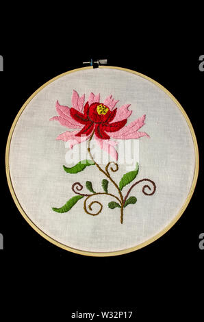Bestickte stilisierte Blume mit roten und rosa Blütenblätter auf Twisted Zweige und Blätter auf weißem Baumwollstoff mit Holz- stickrahmen auf Schwarz hinterg Stockfoto