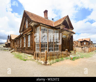 Bodie, Sierra Nevada, Kalifornien, Geisterstadt mit goldenem Ansturm, Haus mit antiken Flaschen, die durch große Fenster sichtbar sind, Zaun mit Pickel, blauer Himmel, weiße Wolken Stockfoto