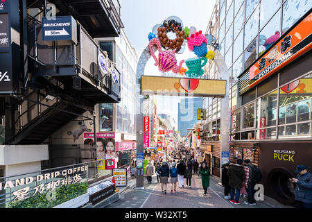 Tokio, Japan - April 2, 2019: Berühmte Takeshita Straße in Harajuku mit Masse von Menschen zu Fuß durch Restaurant shops stores Gebäude durch Eingang arch s Stockfoto