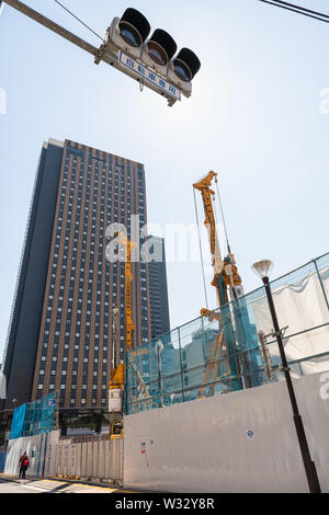 Tokio, USA - April 4, 2019: Stadtteil Shinjuku Station mit Baustellen, Kräne und Menschen zu Fuß auf dem Bürgersteig durch Zaun Wand Stockfoto