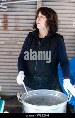 Tokyo, Japan - 30. März 2019: Weibliche Straßenhändler, japanischen Frau kochen Vorbereitung bestand in Topf und Rühren, mit Stäbchen Essen in Tsukiji äußeren heraus Stockfoto