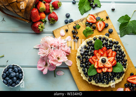 Kuchen mit Beeren Torte mit Erdbeeren und schwarzen Johannisbeeren auf Blau rustikal Tisch. Stockfoto