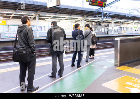 Tokio, Japan - April 4, 2019: Geschäftsleute, Geschäftsmann im Anzug mit Aktentasche und Rucksack stehen in der Linie für shinkansen tra warten Stockfoto