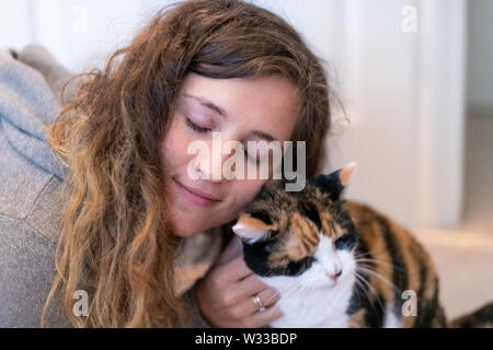 Closeup Portrait von Glücklich lächelnde junge Frau Verklebung mit Calico Cat pet Begleiter, Stoßen, Reiben bunting Köpfe, Freunde Zuneigung zeigen Stockfoto
