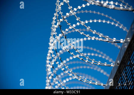 Stacheldraht auf einem Sicherheitszaun mit tiefblauem Himmel hinter Stockfoto