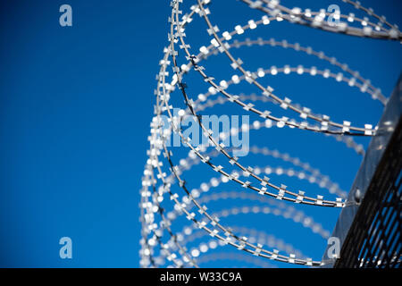 Stacheldraht auf einem Sicherheitszaun mit tiefblauem Himmel hinter Stockfoto