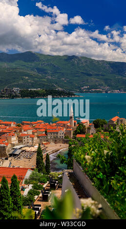 Blick auf die Altstadt von Budva mit der Zitadelle und die Adria in Montenegro auf dem Balkan mit Blumen im Bokeh im Vordergrund. Stockfoto