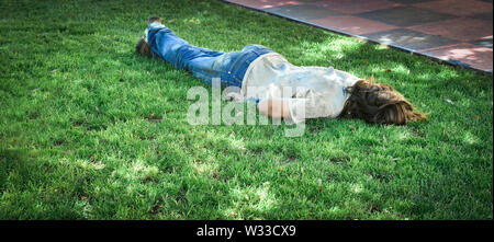 Ein Latina Obdachlosen schläft mit dem Gesicht nach unten auf dem Rasen in einem Park im Sommer Stockfoto