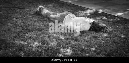 Ein Latina Obdachlosen schläft mit dem Gesicht nach unten auf dem Rasen in einem Park im Sommer, in Schwarz und Weiß Stockfoto
