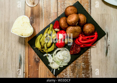 Vorspeisen Vorspeisen sweet cherry mini Paprika gefüllt mit weichem Käse Feta und Zwiebeln auf schiefer Platte. Stockfoto