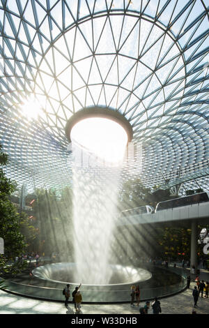 Vertikaler Blick auf den Wasserfall mit Glaskuppeldach von Rain Vortex mit wunderschöner natürlicher Beleuchtung, die in das Innere des Jewel Changi Airport, Singapur, einstrahlt. Stockfoto