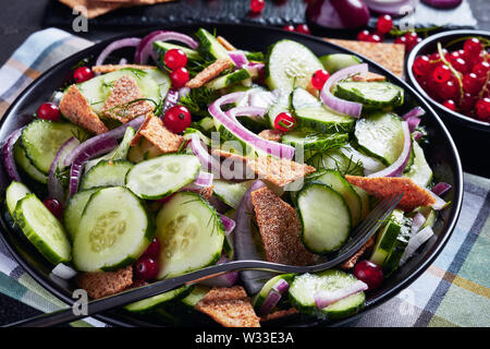 Sommer Gurkensalat mit rote Johannisbeere, marinierte rote Zwiebel und gestochen scharfe Fladenbrot Stücke in einem schwarzen Schüssel Stockfoto