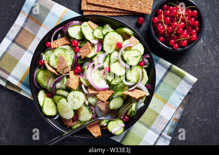 Teil der Köstlichen Sommer Salat aus Gurken, rote Johannisbeere, marinierte rote Zwiebel und gestochen scharfe Fladenbrot Stücke in einem schwarzen Schüssel, Ansicht von oben, flatlay, Stockfoto