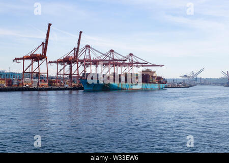 Vereinigte Staaten von Amerika, USA, Washington, Seattle, 11. Mai 2019. Blick vom Wasser auf der Handelshafen mit Kränen und ein großes Containerschiff. Stockfoto