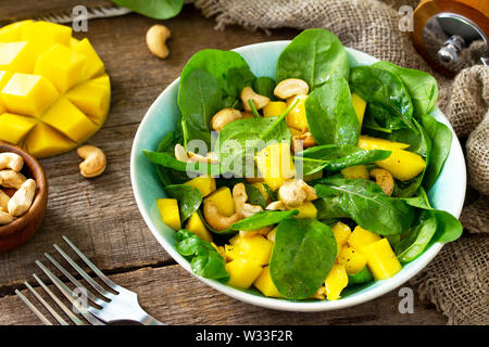 Diätmenü, veganes Essen. Gesunder Salat mit Spinat, Mango, Pecan und vinaigrette Dressing auf einem rustikalen Holztisch. Stockfoto