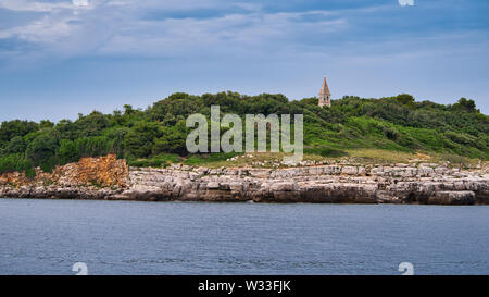 Kleine Insel in der Nähe von Rovinj, Kroatien, mit felsiger Adriaküste, grünem Kiefernwald und einem Kirchturm über dem Meer. Stockfoto