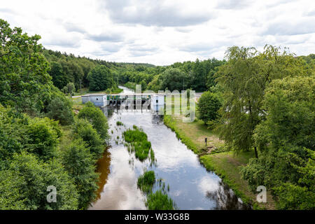 Ein kleines Wasserkraftwerk auf einem kleinen Fluss in Mitteleuropa. Ein Hindernis mit Turbinen zur Stromerzeugung. Jahreszeit des Sommers. Stockfoto