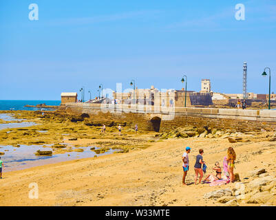 Die Menschen genießen Sie ein Sonnenbad in La Caleta Strand mit dem San Sebastian Castle, eine Festung in La Caleta Insel, im Hintergrund. Cadiz. Spanien. Stockfoto