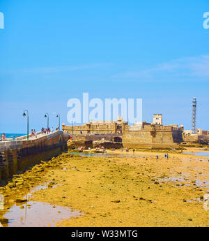 Die Menschen genießen Sie ein Sonnenbad in La Caleta Strand mit dem San Sebastian Castle, eine Festung in La Caleta Insel, im Hintergrund. Cadiz. Spanien. Stockfoto
