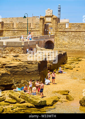 Die Menschen genießen Sie ein Sonnenbad in La Caleta Strand mit dem San Sebastian Castle, eine Festung in La Caleta Insel, im Hintergrund. Cadiz. Spanien. Stockfoto