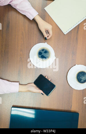 Kaffeepause nach geschäftlichen Verhandlungen. Kaffeepause während der Arbeit im Büro. Tasse Kaffee mit der Hand auf den Tisch, Ansicht von oben. Stockfoto