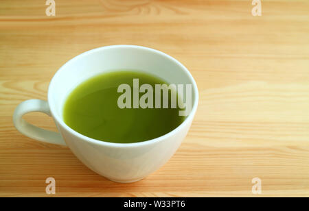 Leuchtende grüne Farbe einer Tasse heißen Matcha Grüntee isoliert auf natürliche braune Holztisch Stockfoto