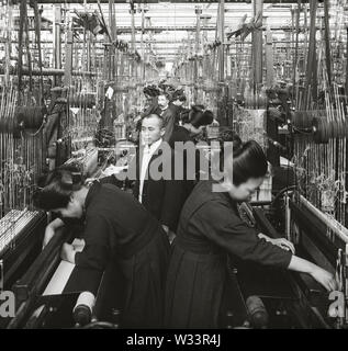 [1900s Japan - Japanische Seide Factory] - ein Mann im Anzug sieht sich als Frauen in Uniform Weben Seide am Kiryu Orimono KK (桐生織物株式会社, Kiryu Textile Company Ltd.), ein japanisches Seidenfabrik in Kiryu, Gunma Präfektur. Das Unternehmen wurde als der Nihon Orimono KK (日本織物株式会社, Japan Textile Company, Ltd.) im Jahre 1887 (Meiji 20). Zu der Zeit als es in Japan war das größte und modernste Seide Fabrik, in den gesamten Prozess der Fertigung von Maschinen getan wurde. 20. Jahrhundert vintage Glas schieben. Stockfoto