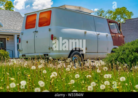 Alte van vor einem Hause unter blauen Himmel mit Wolken an einem sonnigen Tag geparkt. Löwenzahn mit weißen Blumen kann man wächst in den Vordergrund gebracht. Stockfoto