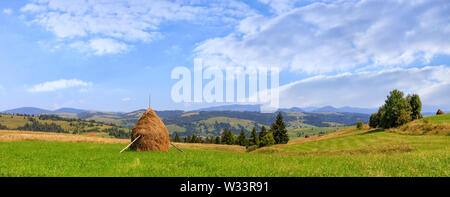 Heuschober auf einer Wiese auf einem Hügel, wunderschöne Berglandschaft auf einem hellen, sonnigen Tag. Panoramaaussicht, Karpaten, Ukraine. Stockfoto