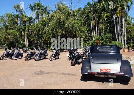 Oldtimer und Motorräder vor einem Palmenhain außerhalb der Corroboree Park Taverne geparkt Stockfoto