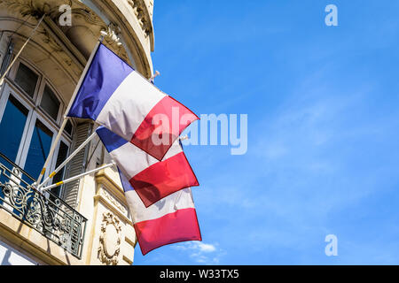 Low Angle View von drei französischen Fahnen schmücken ein Haussmann-gebäude Gebäude in Paris, Frankreich, an einem sonnigen Sommertag. Stockfoto