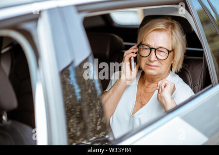 Senior Business Frau im Gespräch mit Telefon, während sitzen auf dem Rücksitz des modernen Auto. Konzept einer Geschäft Leben im Ruhestand Stockfoto