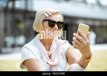 Schöne und elegante ältere Frau mit Smartphone im Freien in der Stadt. Konzept eines aktiven Geschäftsleben auf Ruhestand Stockfoto