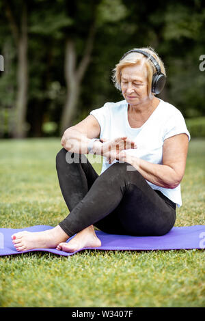 Ältere Frau suchen, die auf dem Smart beobachten, während Yoga im Freien. Konzept für einen gesunden Lebensstil im Ruhestand Stockfoto