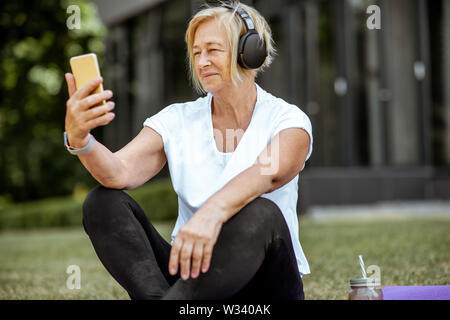 Gerne ältere Frau unter selfie Foto beim Üben von Yoga im Freien. Konzept für einen gesunden Lebensstil im Ruhestand Stockfoto
