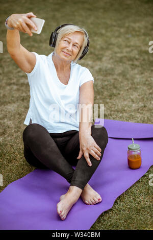 Gerne ältere Frau unter selfie Foto beim Üben von Yoga im Freien. Konzept für einen gesunden Lebensstil im Ruhestand Stockfoto