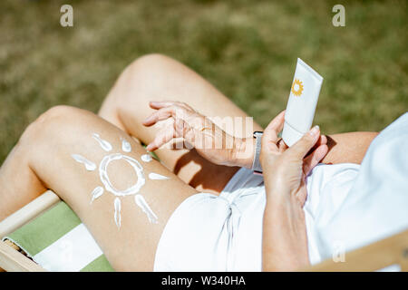 Ältere Frau mit Sun Form auf ihr Bein aus Sonnencreme, ein Rohr mit Sahne, während er im Freien Stockfoto