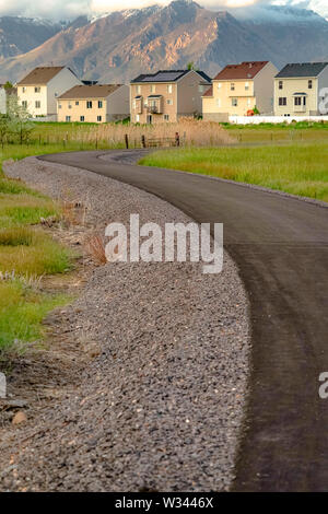 Straße, die zu den schönen mehrstöckige Häuser mit Berg im Hintergrund führt. Die asphaltierte Straße führt durch das exansive grasbewachsenen Gelände. Stockfoto