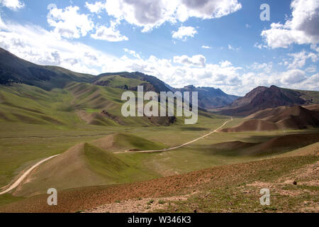 Mountain Road, zwischen den malerischen Hügeln gegen den blauen Himmel mit weißen Wolken. Reisen. Kirgisistan. Stockfoto