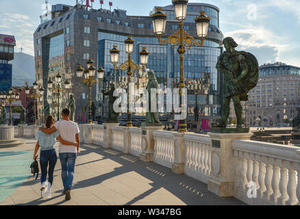 SKOPJE, MAZEDONIEN - 23. AUGUST 2019: ein paar Gehminuten umarmte, vorbei an prunkvollen Statuen, über eine Brücke in Richtung Mazedonien Square führt. Stockfoto