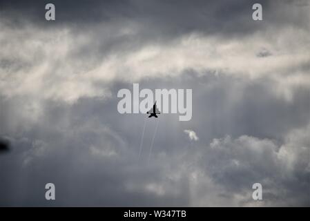 F15 Jet fighter in der Ferne in ein dunkles Grau bewölkter Himmel mit Sonnenlicht strahlen scheint von oben nach unten und neben dem Flugzeug Stockfoto
