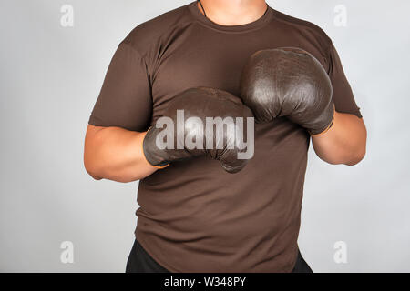 Junge Mann steht in einem Rack, das Tragen von sehr alten Vintage Brown Boxhandschuhe auf seinen Händen, weißer Hintergrund Stockfoto