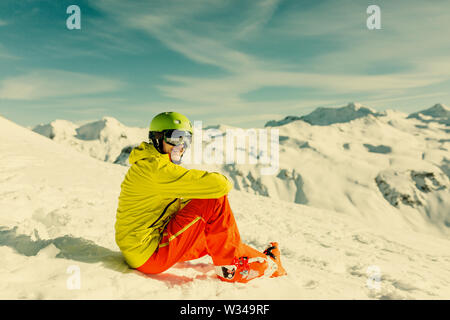 Bild von sportlichen Mann mit Helm tragen gelbe Jacke sitzen auf schneebedeckten Hang Stockfoto