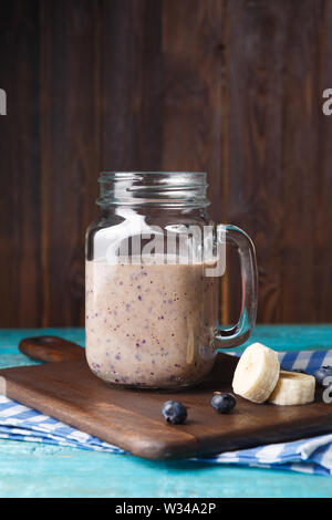 Bild von Becher mit milchshake mit Banane und Beeren auf schneidebrett an der hölzernen Hintergrund Stockfoto