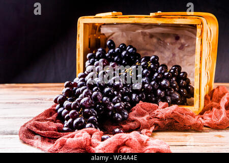 Bild von oben von schwarzen Trauben in Holz- korb mit weinroten Tuch Stockfoto