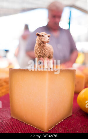 Nahaufnahme der Organischen spanischer Ziegenkäse Stück mit Ziege statuette und Landwirt im Hintergrund, im Outdoor Street Food Markt an einem sonnigen Sommertag Stockfoto