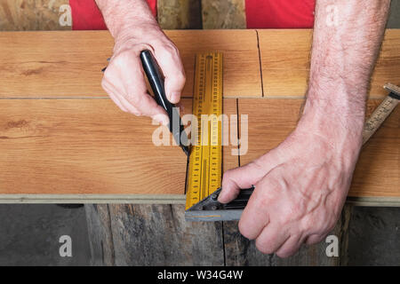 Die Hände des Arbeiters Mark ein Laminat mit Hilfe eines Lineals, ein Quadrat und ein Filzstift. Der master Arbeiter im roten Overall bereitet das Laminat Stockfoto