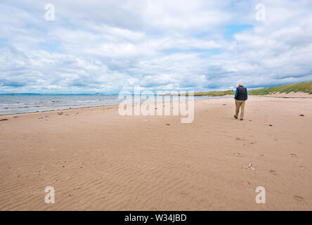 Aberlady Coastal Nature Reserve, East Lothian, Schottland, Vereinigtes Königreich, 12. Juli 2019. UK Wetter: Wandern im Naturschutzgebiet an einem sonnigen Tag. Ein älterer Mann Spaziergänge entlang der leeren Strand entlang am Ufer des Firth von weiter Stockfoto