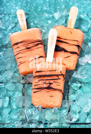 Hausgemachte Eis am Stiel von zuckermelone mit Schokolade und Eiswürfel auf hellem rustikalen türkis Hintergrund. Stockfoto