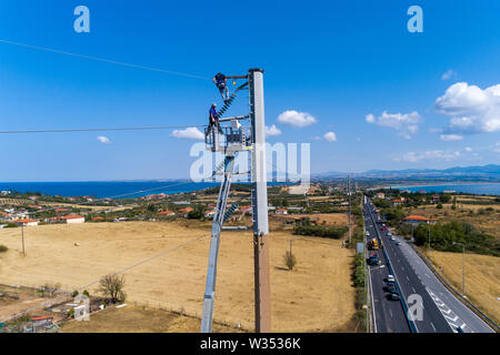 Chalkidiki, Griechenland - Juli 12, 2019: Elektriker sind Klettern auf elektrischen Polen Stromleitungen zu installieren und reparieren Nach dem heftigen Sturm, t Struck Stockfoto